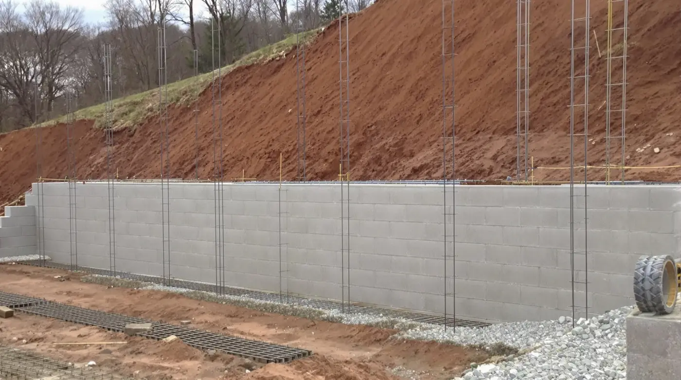 Retaining wall drainage and waterproofing detail showing French drain, membrane, and granular backfill in Kansas City